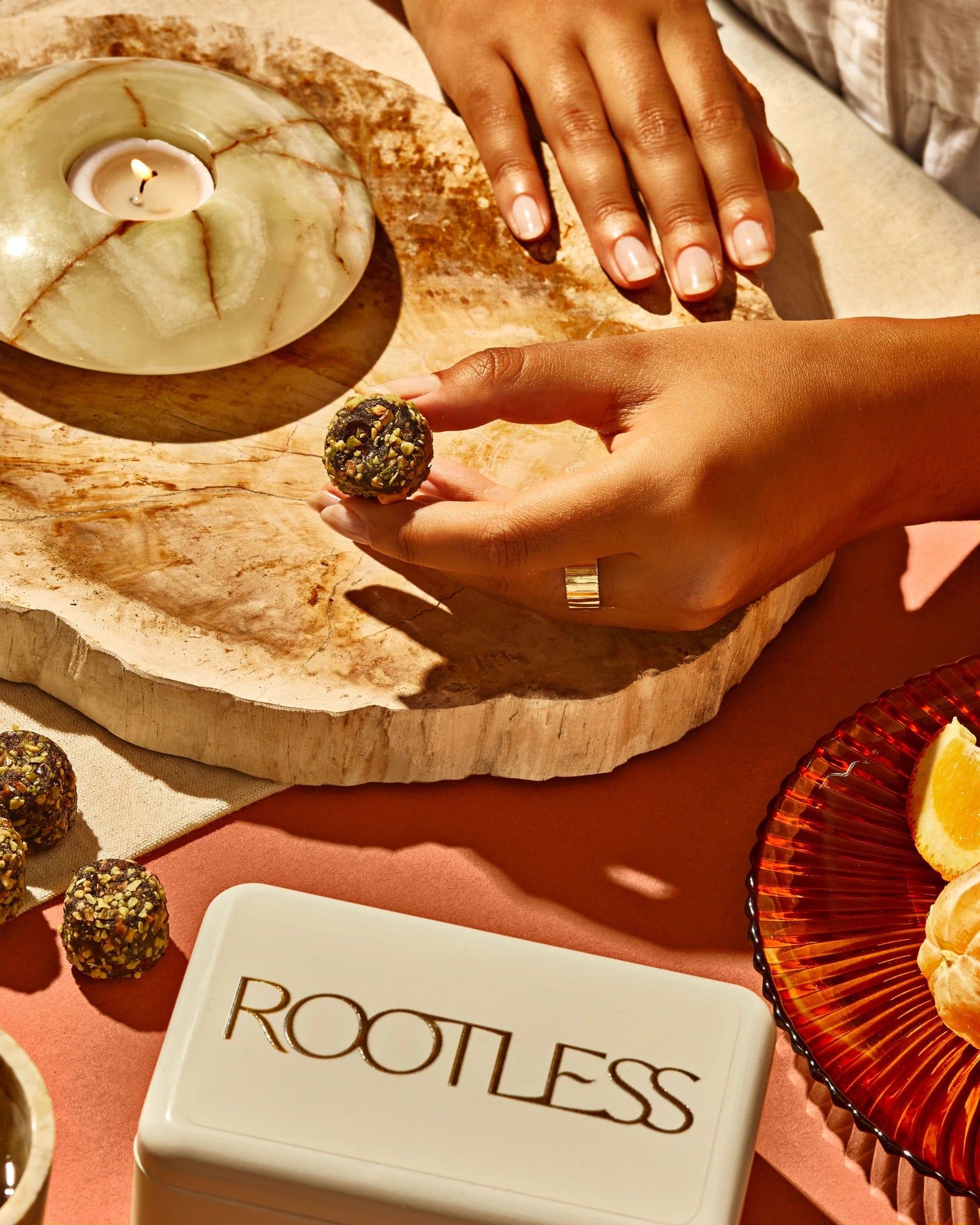 An Orange Pistachio Daily Bite held beside a Rootless tin and fresh orange
